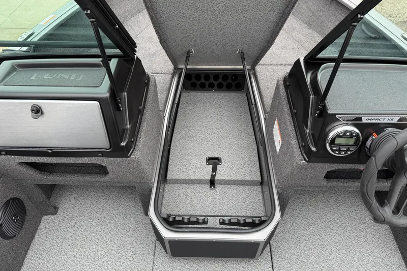 Slide: The Image of 2026 Lund 1875 Impact XS Sport boat interior with open storage compartment and dashboard controls. - 18