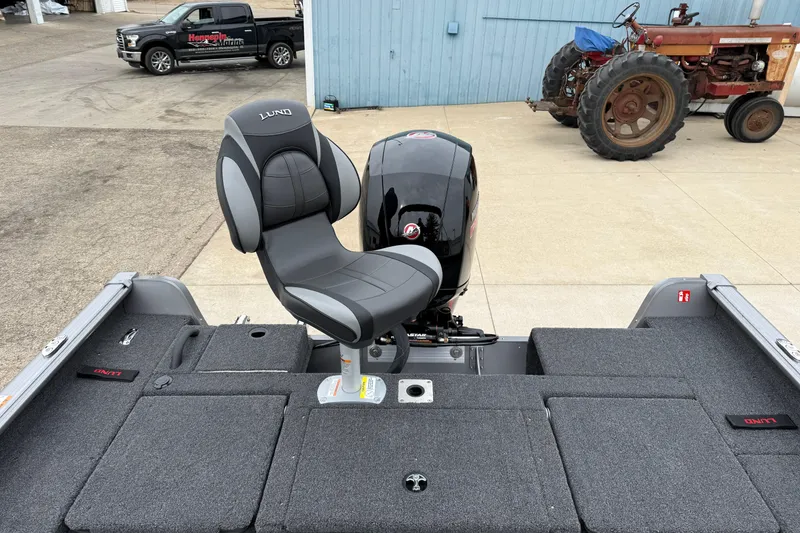 Slide: The Image of 2026 Lund 1875 Impact XS Sport boat with cushioned seat and motor, parked outdoors. - 34