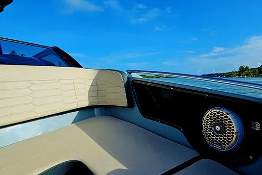 Slide: The Image of 2025 NX Boats NX260 interior with beige seating and speaker, under clear blue sky. - 12