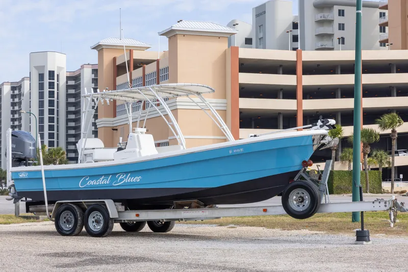 Slide: The Image of 2017 Andros Tarpon 26 boat on trailer, labeled "Coastal Blues," with modern buildings in background. - 2