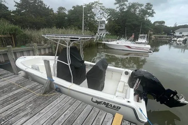 Slide: The Image of 2021 Mako 214 Center Console boat docked by a wooden pier in a serene marina. - 2