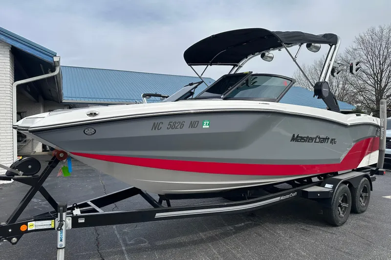 Slide: The Image of 2023 MasterCraft NXT22 boat on trailer, gray and red design, parked outdoors. - 2