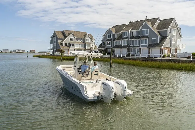 Slide: The Image of A 2026 Sailfish 252 CC boat navigates calm waters near coastal houses. - 23