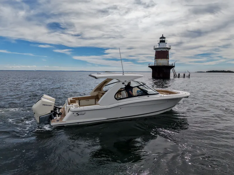 Slide: The Image of A 2027 Scout 288 Dorado boat cruises on calm waters past a lighthouse. - 8