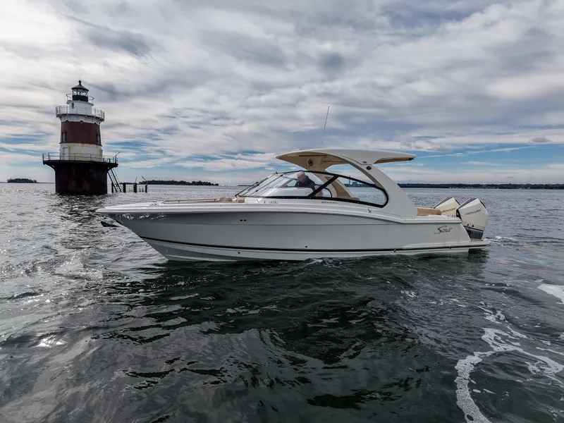 Slide: The Image of A 2027 Scout 288 Dorado boat on the water, with a lighthouse in the background. - 2
