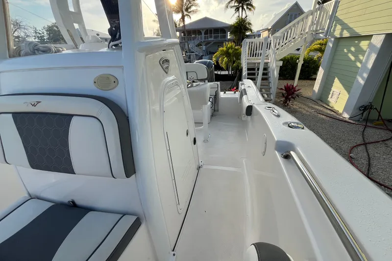 Slide: The Image of 2017 Tidewater 230 CC Adventure boat interior with seating and console, docked near tropical homes. - 10