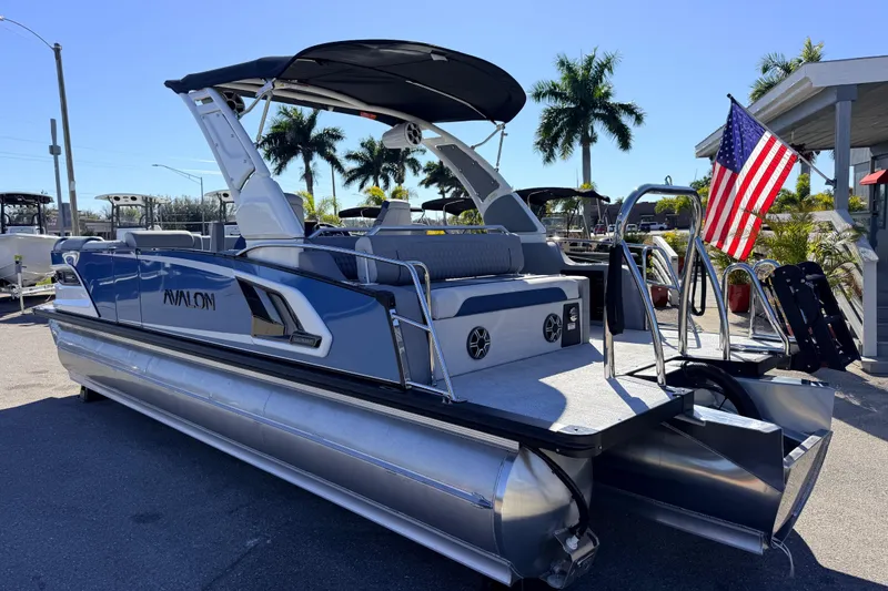 Slide: The Image of 2026 Avalon 2585 Excalibur LTD Flex Lounge Tri Toon boat with American flag, parked outdoors. - 10
