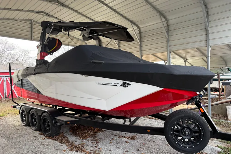 The Image of 2023 Nautique Super Air Nautique G23 boat, covered, on a trailer in a sheltered area. - 1