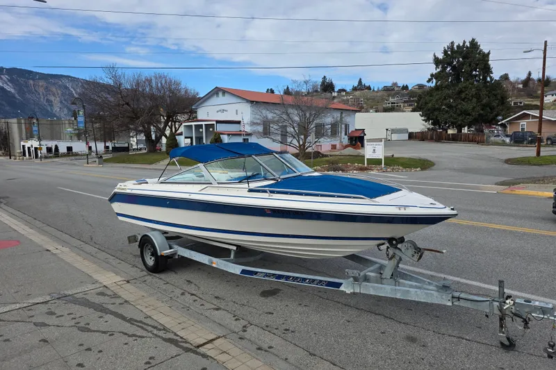 Slide: The Image of 1990 Sea Ray 210 Bow Rider on trailer, parked on street with scenic background. - 3