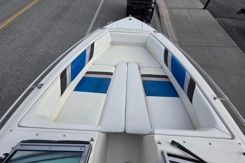 Slide: The Image of 1990 Sea Ray 210 Bow Rider boat with white and blue seating, docked on pavement. - 7