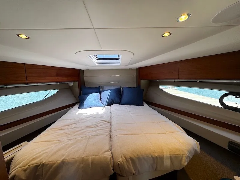 Slide: The Image of The 2020 Princess V50 cabin features a cozy double bed with blue pillows and wood paneling. - 36