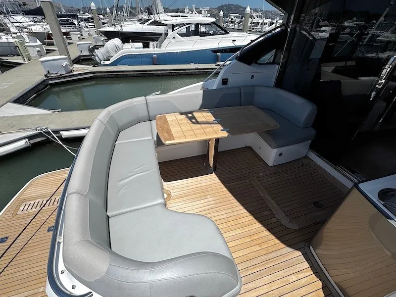Slide: The Image of The image shows the aft deck of a 2020 Princess V50 boat with a U-shaped seating area and wooden table on a teak deck. - 10