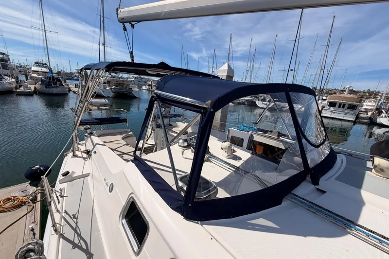 Slide: The Image of 2007 Hunter 44 Deck Salon sailboat docked in marina, featuring blue canopy and clear windows. - 20