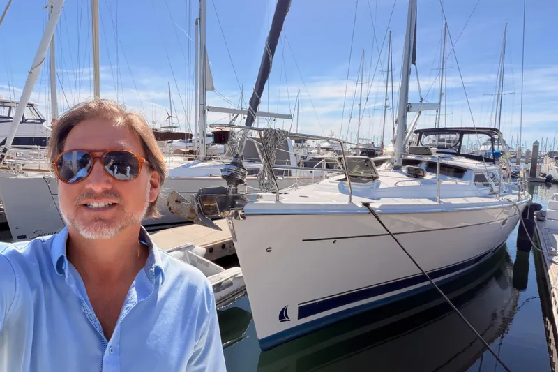 Slide: The Image of Man smiling beside a 2007 Hunter 44 Deck Salon yacht in a marina. - 5