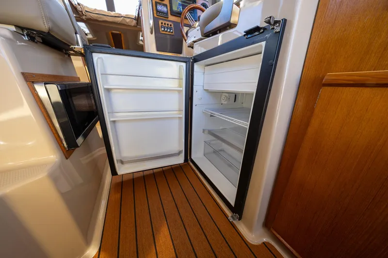 Slide: The Image of 2019 Ranger Tugs R-23 interior with open refrigerator and wooden flooring. - 20