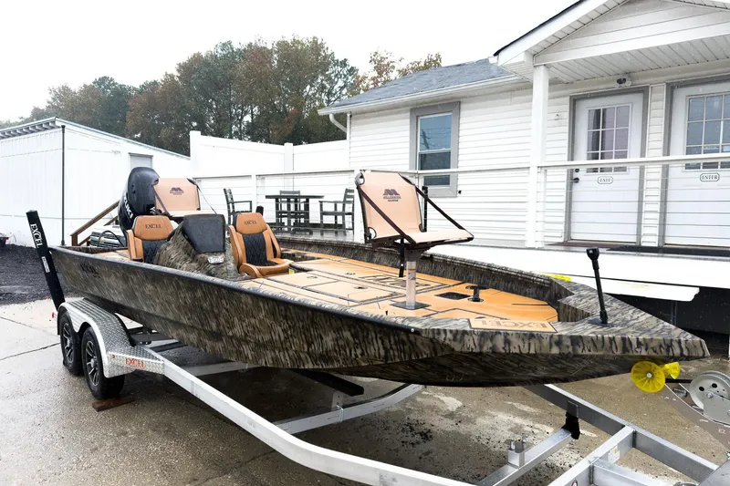 Slide: The Image of 2026 Excel EX203C Crappie & Bass boat on trailer, camo design, parked near white building. - 6