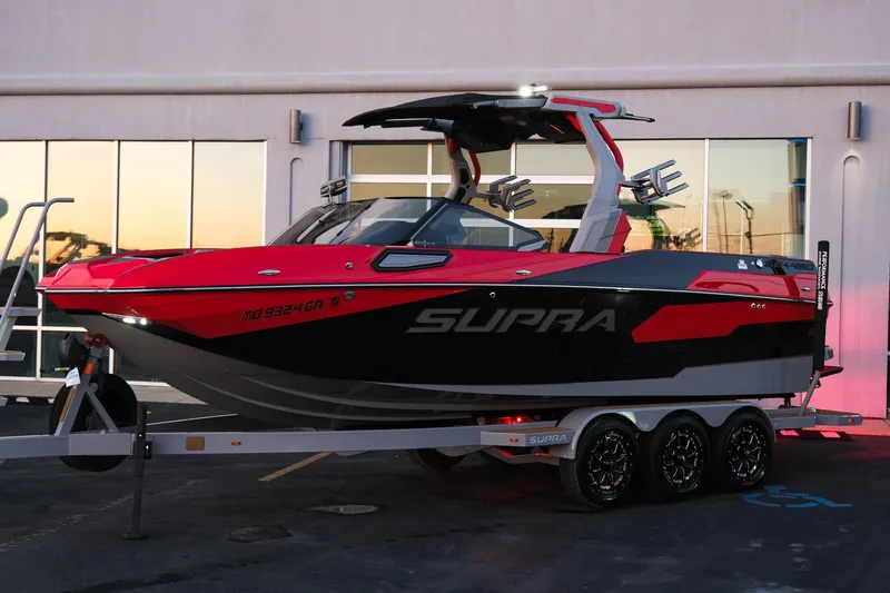Slide: The Image of 2025 Supra SE boat in red and black on a trailer, parked outside a building. - 10