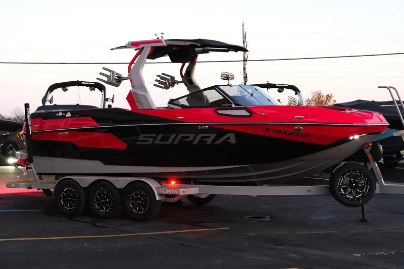 Slide: The Image of 2025 Supra SE boat in red and black on a trailer at sunset. - 11