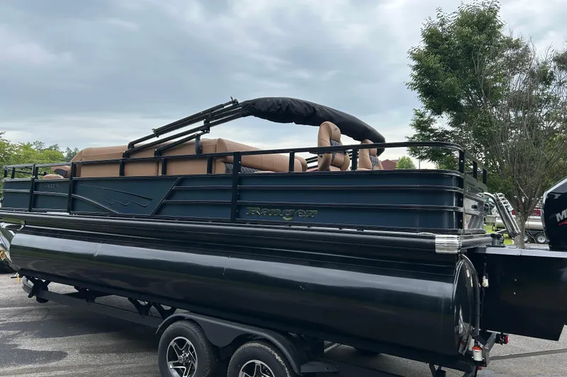 Slide: The Image of 2026 Ranger 223F pontoon boat on trailer, parked outdoors under cloudy sky. - 2