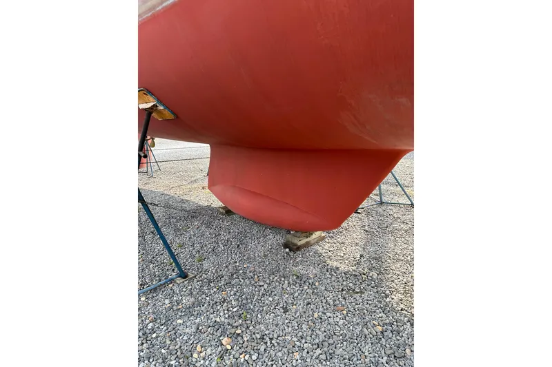 Slide: The Image of Red hull of a 2000 Outbound 44 sailboat on gravel, supported by stands. - 77