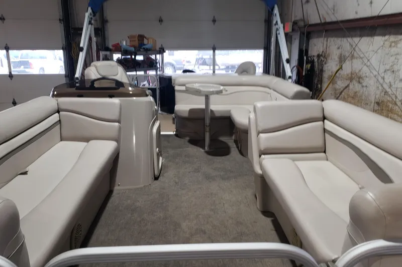 Slide: The Image of 2014 Bennington 22SSX pontoon boat interior with beige seating and table in a garage. - 3
