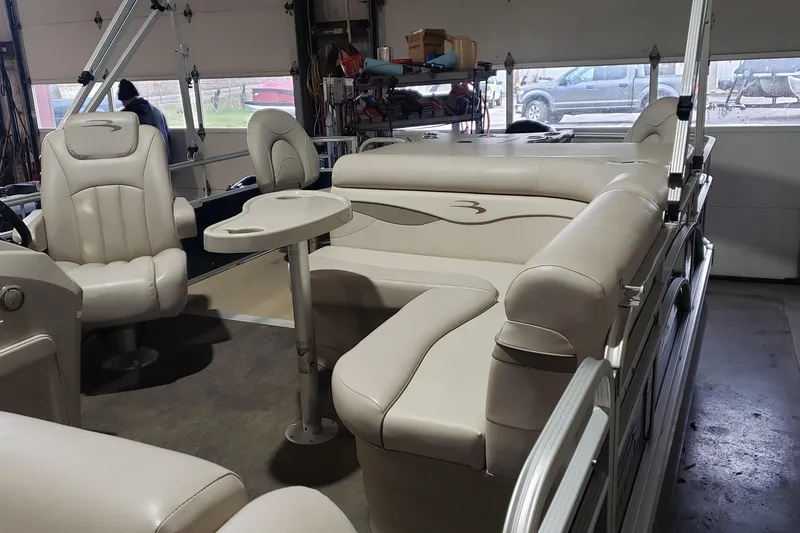 Slide: The Image of 2014 Bennington 22SSX pontoon boat interior with beige seating and table in a garage. - 4
