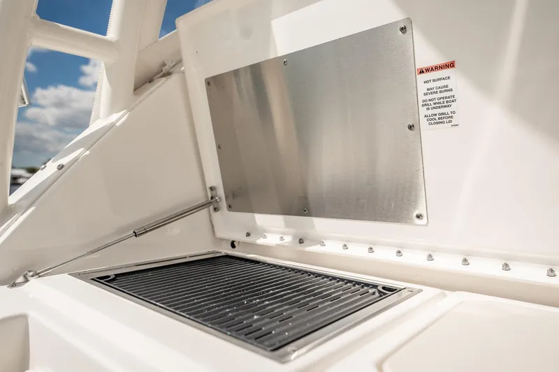 Slide: The Image of 2024 Pursuit OS 325 Offshore boat grill area with safety warning label. - 16