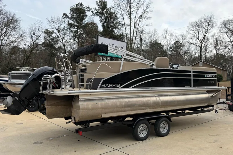 Slide: The Image of 2025 Harris Cruiser 230 pontoon boat on trailer, parked outdoors. - 2