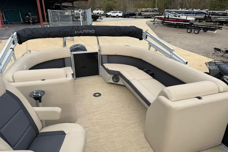Slide: The Image of 2025 Harris Cruiser 230 pontoon boat with beige seating and black accents, docked outdoors. - 7