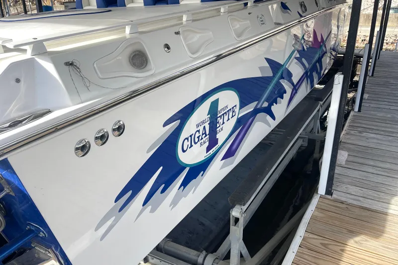 Slide: The Image of 1998 Cigarette 38' Top Gun boat with vibrant graphics docked on a wooden pier. - 10
