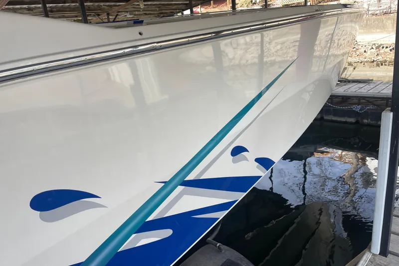 Slide: The Image of 1998 Cigarette 38' Top Gun boat with sleek blue and teal graphics, docked in water. - 6