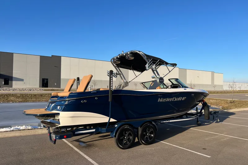 Slide: The Image of 2022 MasterCraft XT25 boat on trailer in parking lot, clear blue sky background. - 4