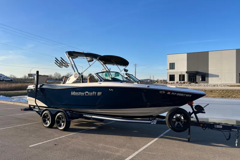 Slide: The Image of 2022 MasterCraft XT25 boat on trailer, parked outdoors under clear blue sky. - 5
