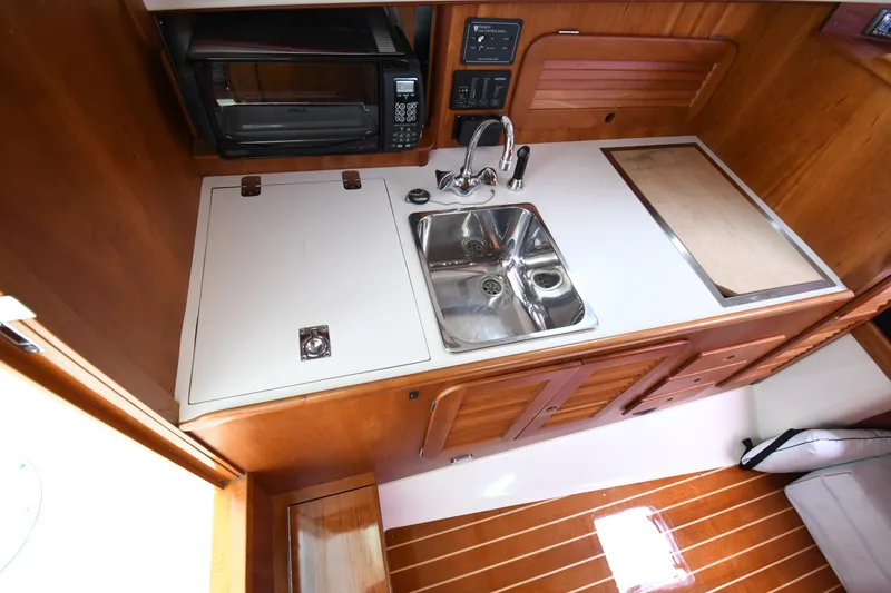 Slide: The Image of 2005 Hinckley Picnic Boat 36 EP galley with sink, microwave, and wooden cabinetry. - 26