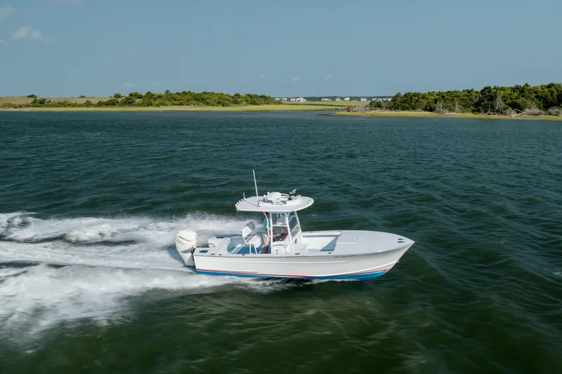 Slide: The Image of 2019 Gamefisherman 26 Cuddy Cabin cruising on open water near a scenic shoreline. - 51