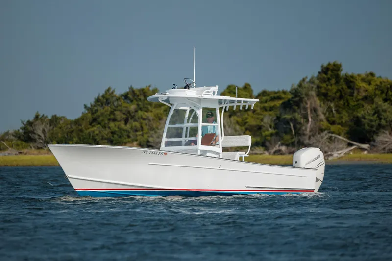 Slide: The Image of 2019 Gamefisherman 26 Cuddy Cabin boat cruising on water near lush shoreline. - 6