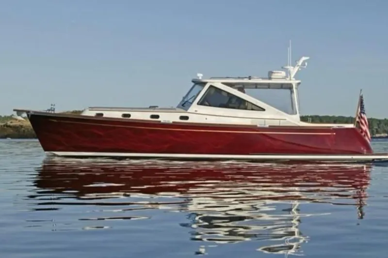 The Image of 2005 Lyman-Morse Monhegan boat on calm water, featuring a sleek red hull. - 0