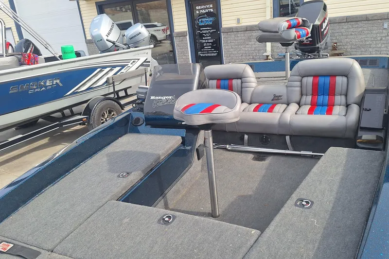 Slide: The Image of 1994 Ranger 481VS boat interior with gray and red-striped seating, parked near a Smoker Craft boat. - 5