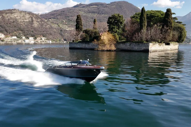 Slide: The Image of 2025 Riva boat cruising on a serene lake near a small island with lush greenery. - 8