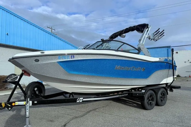 Slide: The Image of 2023 MasterCraft XT22 boat on trailer, blue and white design, parked outdoors. - 4