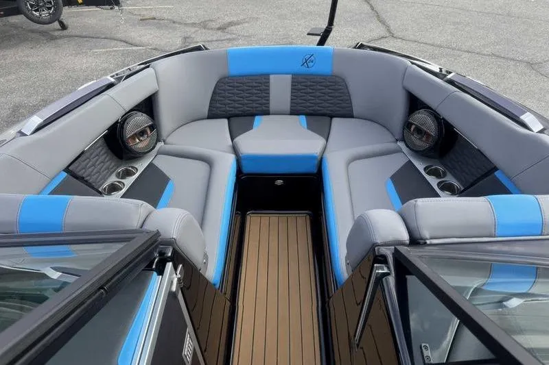 Slide: The Image of 2024 MasterCraft X24 boat interior with gray and blue seating, cup holders, and speakers. - 12