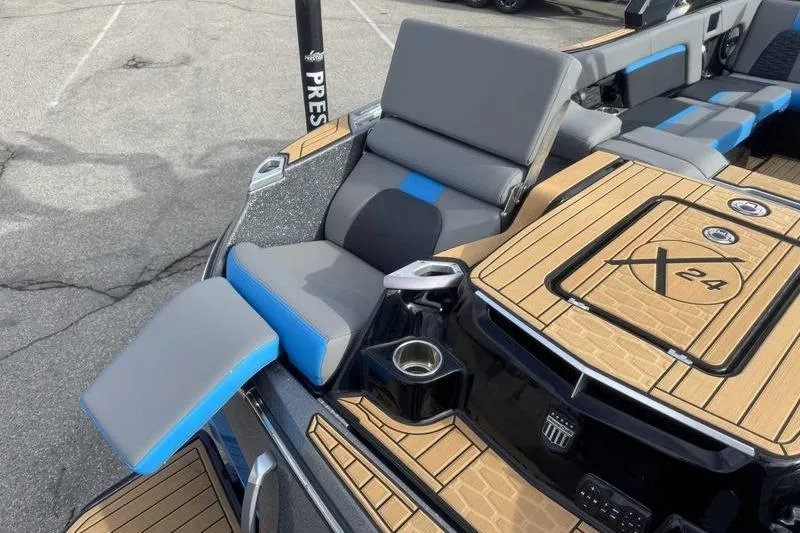 Slide: The Image of 2024 MasterCraft X24 boat interior with gray and blue seating, cup holders, and teak-style flooring. - 14