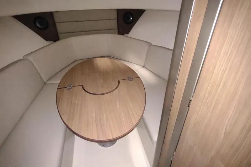 Slide: The Image of 2015 Boston Whaler 285 Conquest cabin interior with round wooden table and cushioned seating. - 44
