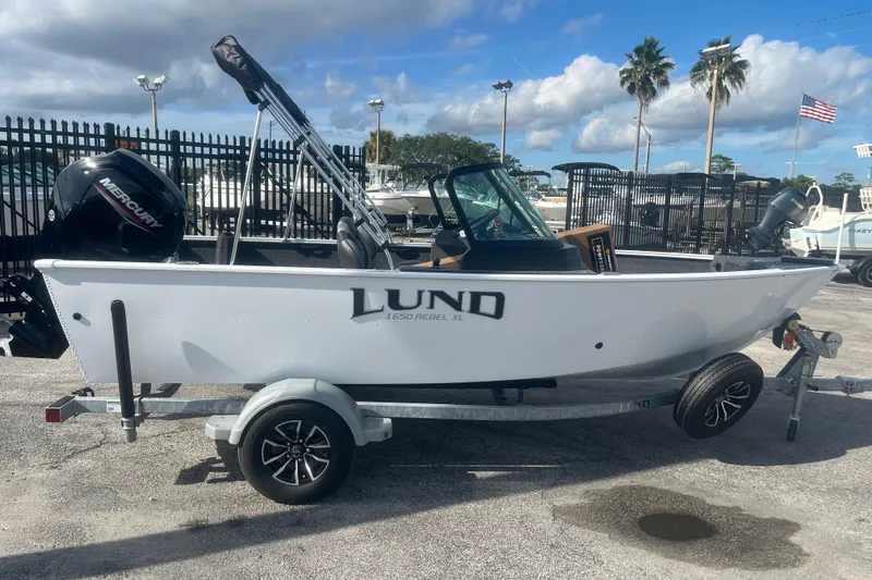 Slide: The Image of 2026 Lund 1650 Rebel XL Sport boat on trailer, parked outdoors under blue sky. - 2