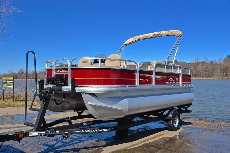 Slide: The Image of 2024 Sun Tracker Bass Buggy 18 DLX pontoon boat on trailer by a lake. - 10