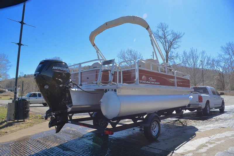 Slide: The Image of 2024 Sun Tracker Bass Buggy 18 DLX pontoon boat on trailer, parked outdoors. - 14