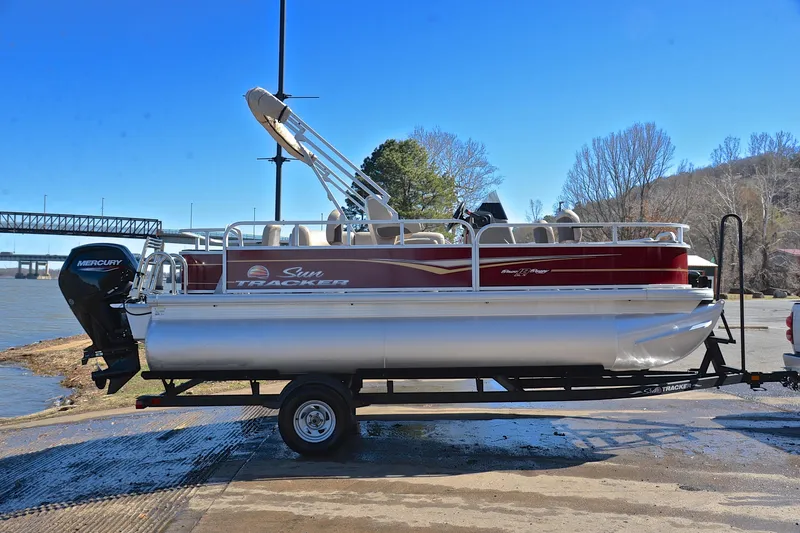 Slide: The Image of 2024 Sun Tracker Bass Buggy 18 DLX pontoon boat on trailer by a river. - 15