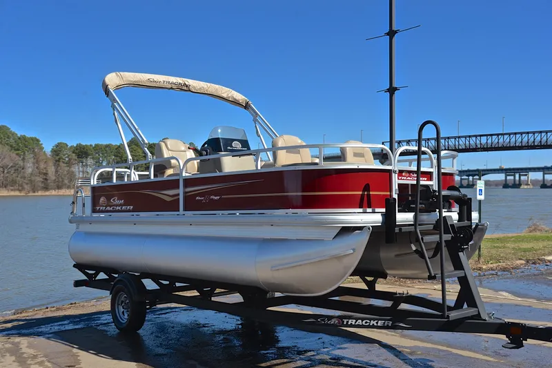 Slide: The Image of 2024 Sun Tracker Bass Buggy 18 DLX pontoon boat on trailer by a lake. - 16