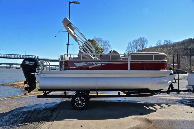 Slide: The Image of 2021 Ranger 180 Reata pontoon boat on trailer by riverside, clear blue sky. - 15