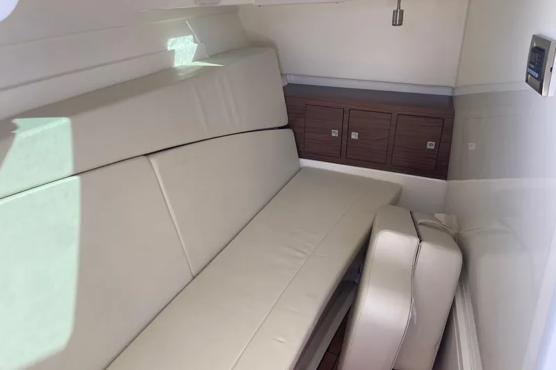 Slide: The Image of 2024 Boston Whaler 320 Vantage cabin interior with beige seating and wooden storage cabinets. - 37